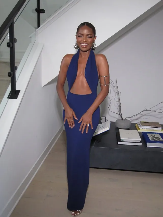 Ryan Destiny posing beside stairs in a long blue dress and heels.