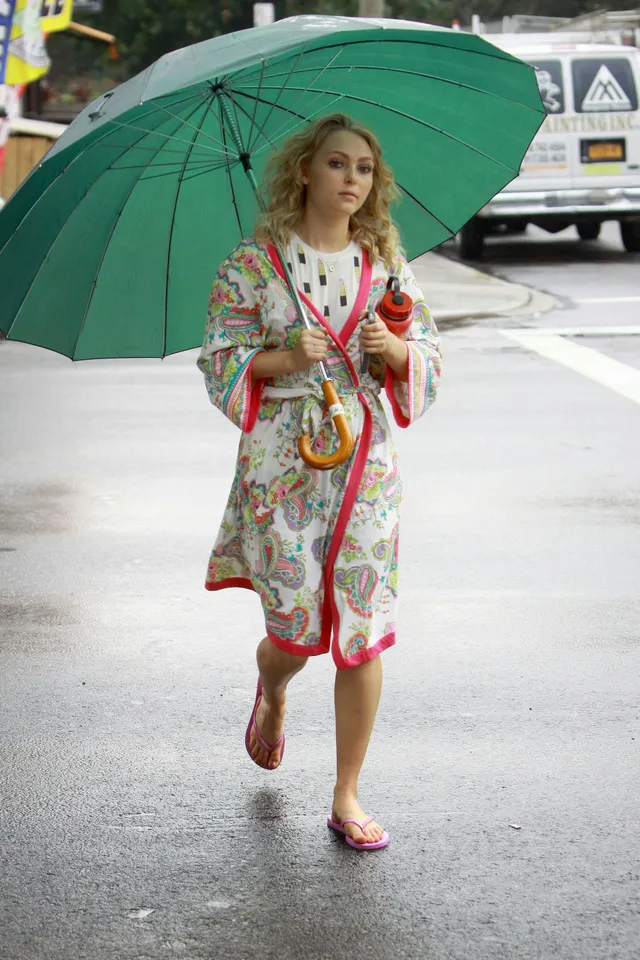 AnnaSophia Robb walking beneath a green umbrella in a patterned robe.