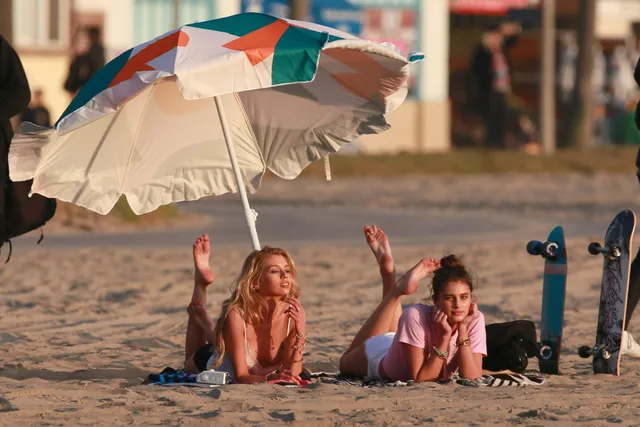 Taylor Hill relaxing barefoot on a beach with a companion beneath a parasol.