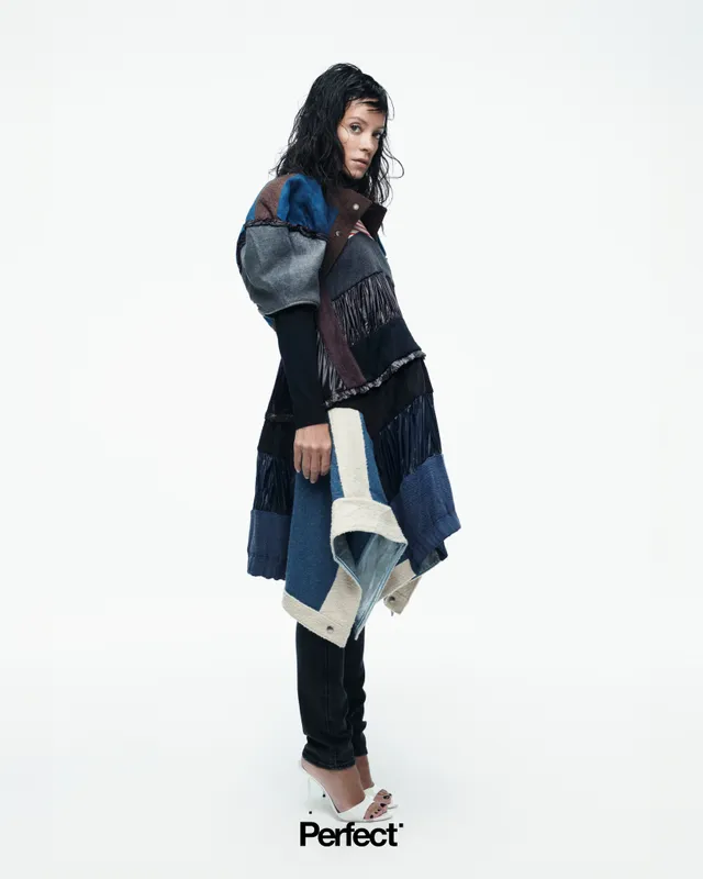 Lily Allen posing in a layered outfit and white heels for a studio portrait.