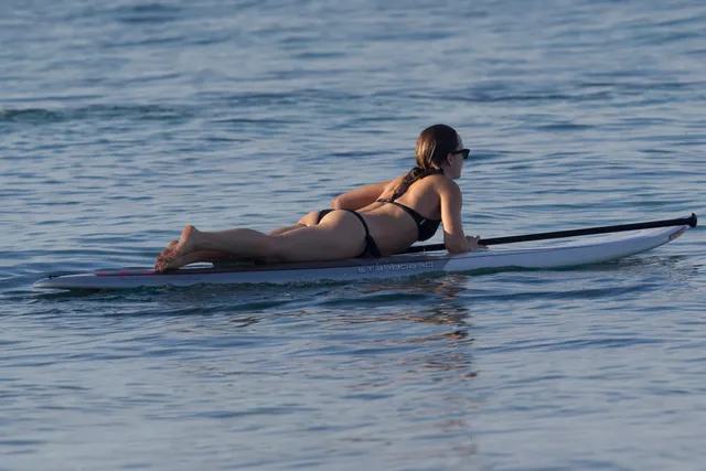 Olivia Wilde lying barefoot on a paddleboard on the water.