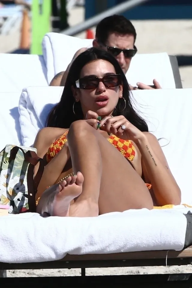 Dua Lipa: relaxing barefoot on an outdoor lounger in an orange swimsuit.