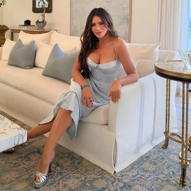 Sofía Vergara sitting on a pale sofa in a blue dress and silver heels.