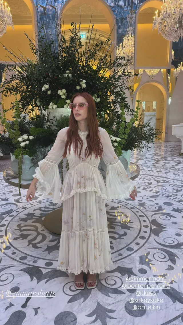 Emma Roberts posing in a long cream dress in an ornate interior.