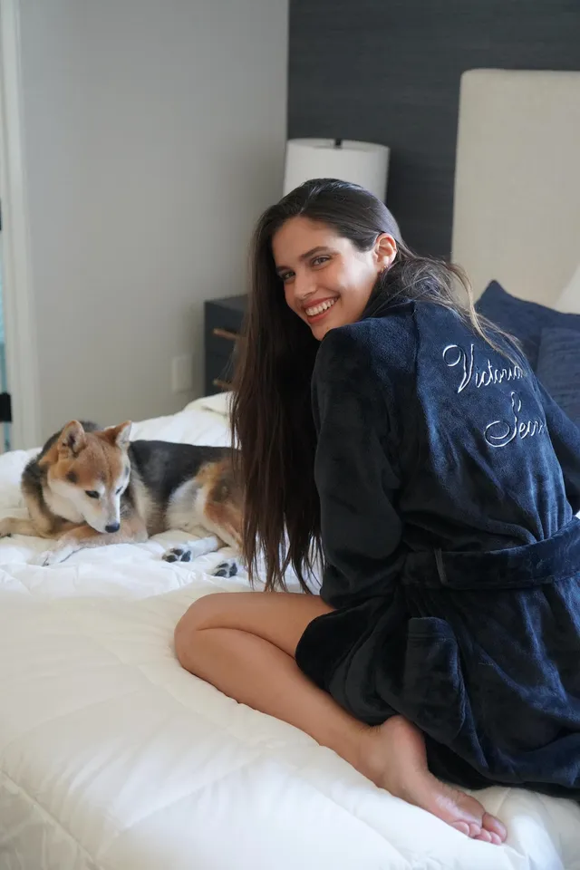 Sara Sampaio sitting barefoot on a bed beside a dog.