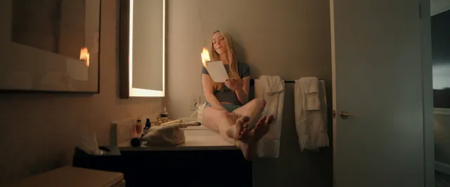 Amanda Seyfried sitting barefoot on a bathroom counter in a screen image.