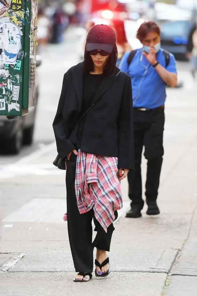 Zoë Kravitz walking outdoors in a dark outfit and flat sandals.