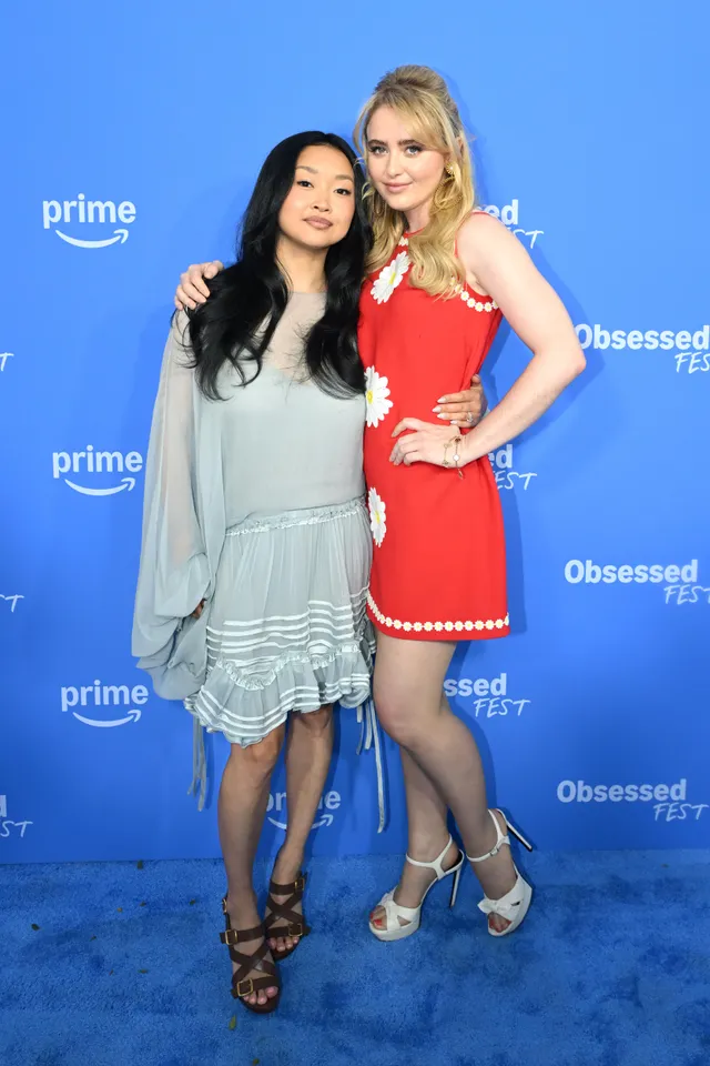 Kathryn Newton posing beside another woman in a red dress and pale heels.