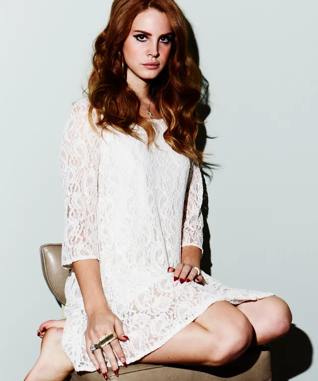 Lana Del Rey sitting cross-legged in a white dress.
