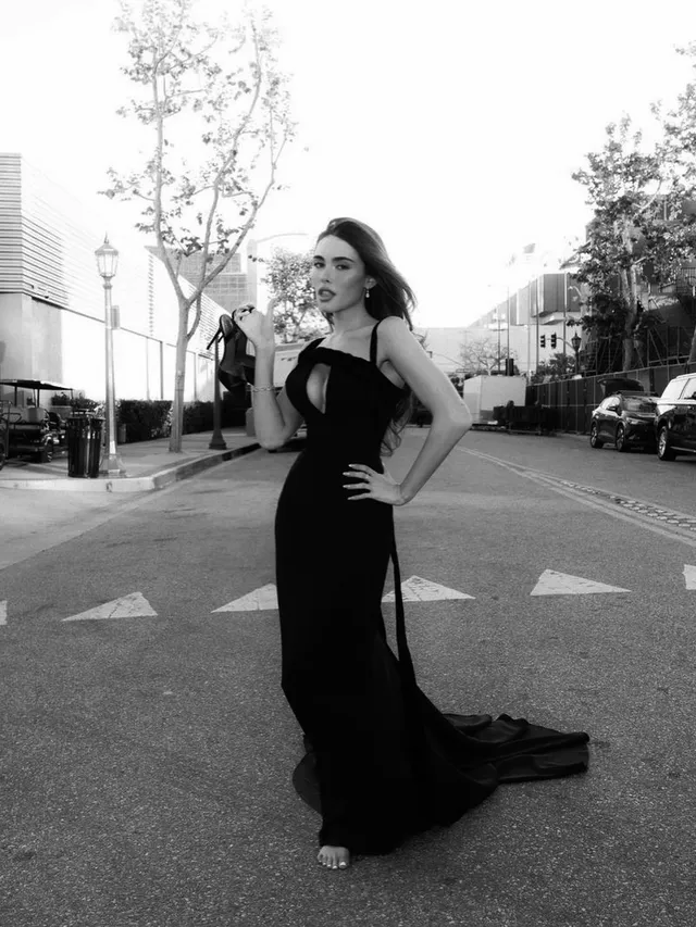 Madison Beer posing outside in a long black gown and heels for a monochrome photograph.