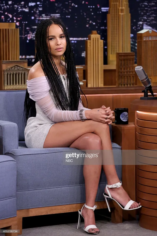 Zoë Kravitz sitting on a talk show sofa in a pale dress.