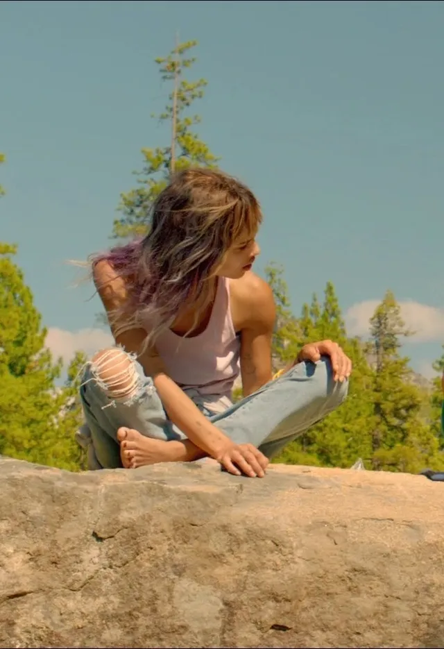 Zoë Kravitz sitting on a rock outdoors in jeans.