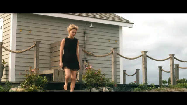 Emily Alyn Lind standing barefoot outside a small building in a black dress.