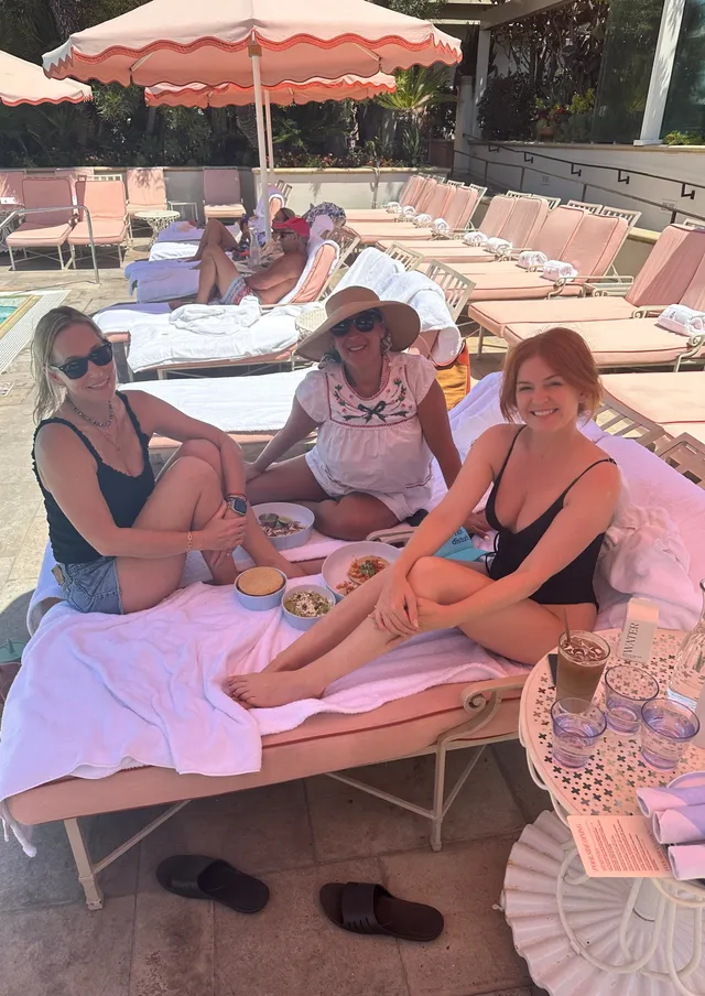 Isla Fisher relaxing beside companions on a poolside lounger.