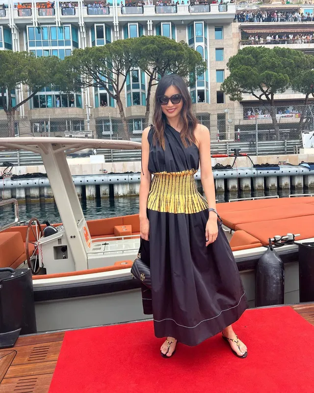 Gemma Chan standing on a boat in a long skirt and flat sandals.