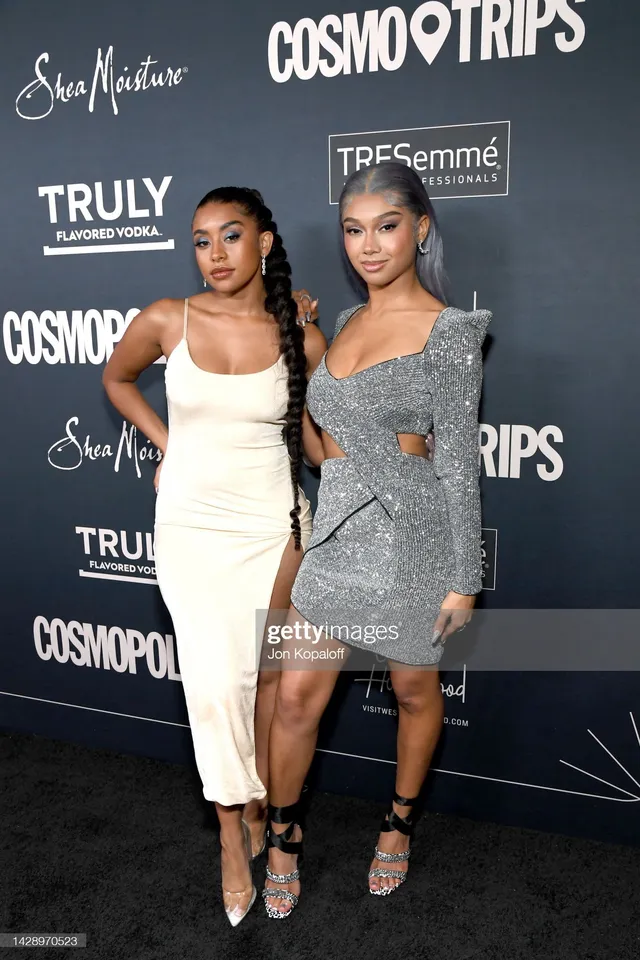 Sierra Capri posing beside a guest in a pale dress and black heels at an event.