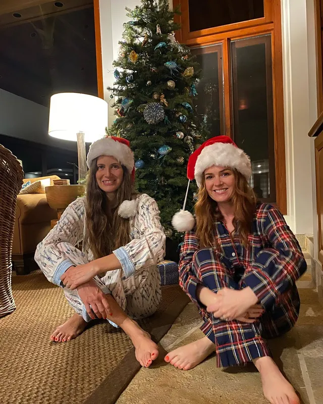 Isla Fisher sitting with a companion beside a Christmas tree.