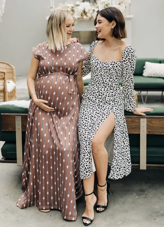Lucy Hale posing beside a companion in a patterned dress and black heels.