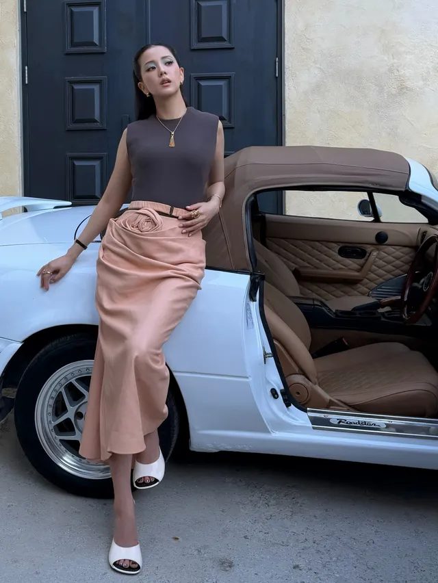 Jisoo wearing white peep-toe heels with a satin skirt beside a vehicle.