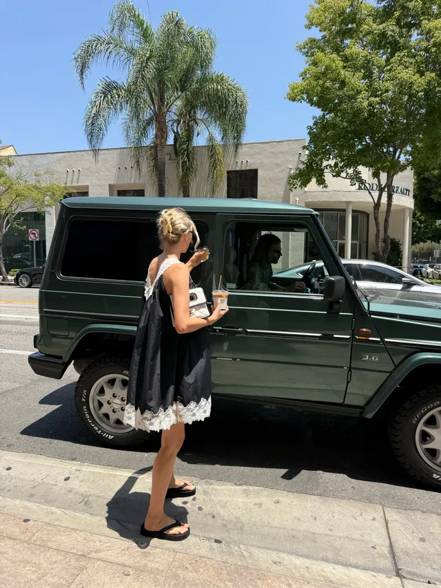 Elsa Hosk standing beside a vehicle in black flat sandals and a black dress.
