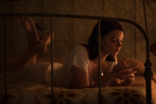 Anya Taylor-Joy seated on a bed in a warmly lit screen scene.