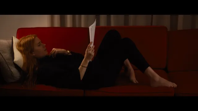Amy Adams reclining on a sofa reading a book.