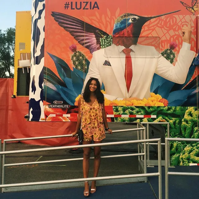 Greta Onieogou standing before a colorful mural in a patterned dress and flat sandals.