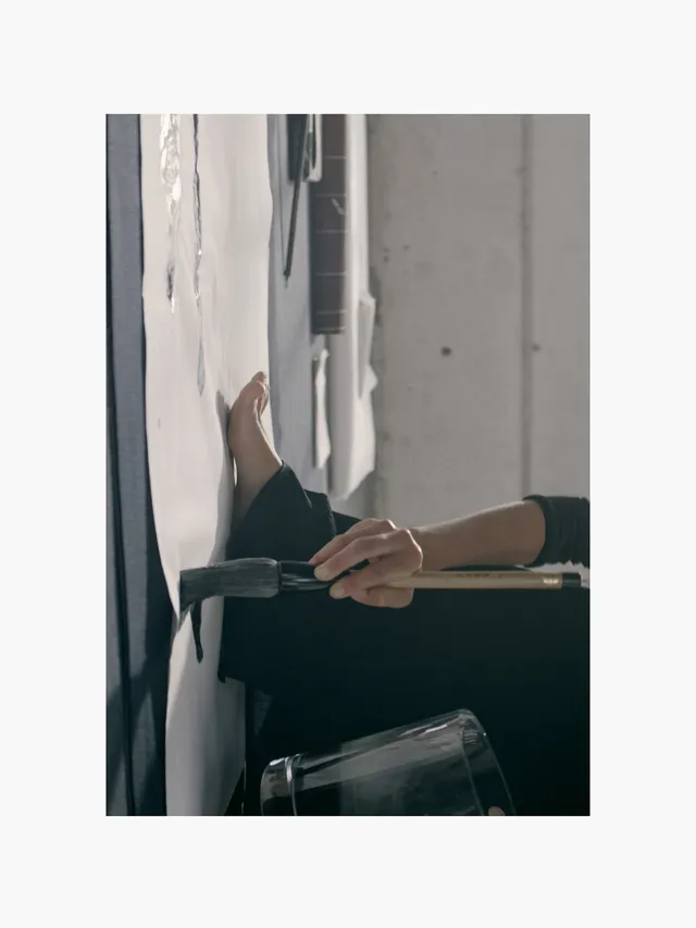 Adria Arjona reclining with one leg raised against a wall.