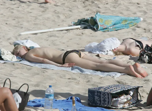 Kirsten Dunst lying on a beach towel in a black swimsuit.