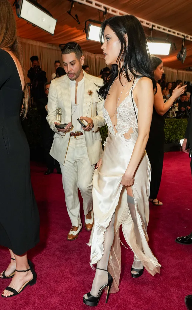 Jenna Ortega wearing a pale gown and metallic heels on a red carpet.