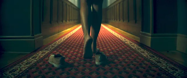 Ester Expósito showing her bare feet in a dimly lit hallway scene.