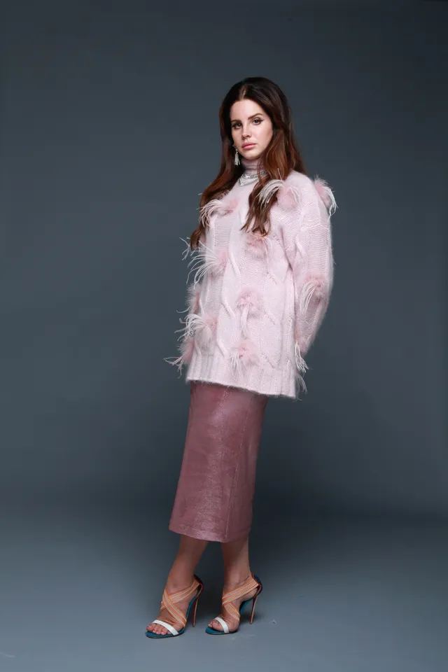 Lana Del Rey posing in a pale jacket, long skirt and heels.
