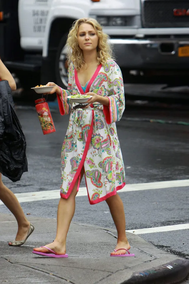 AnnaSophia Robb standing beside a vehicle in a patterned robe and flip-flops.