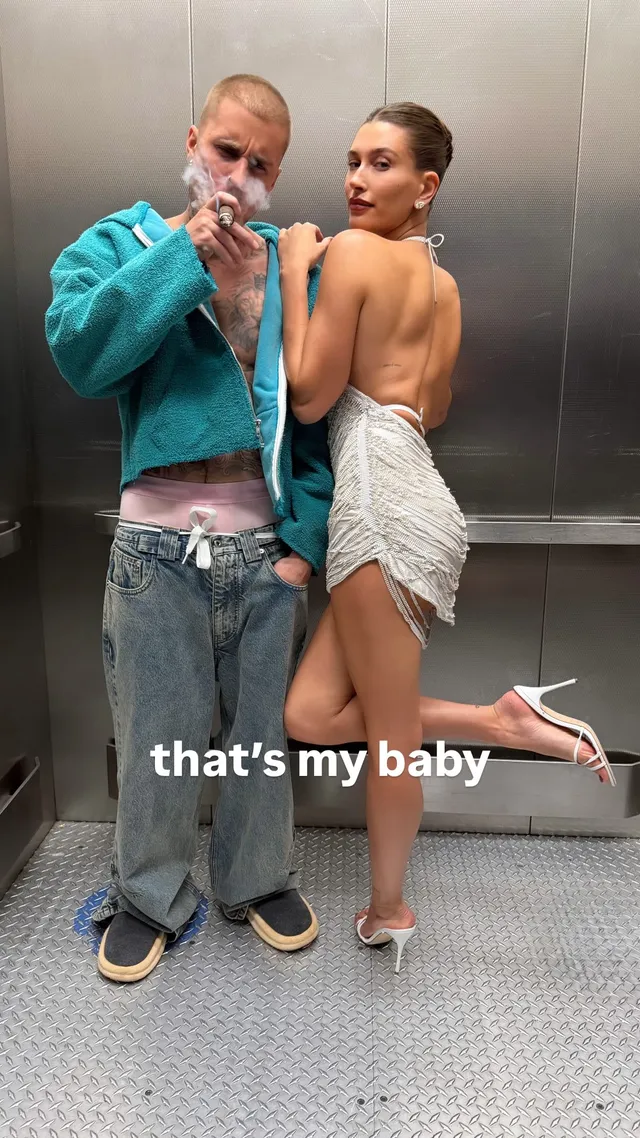 Hailey Bieber posing beside another person in a pale dress and heels.