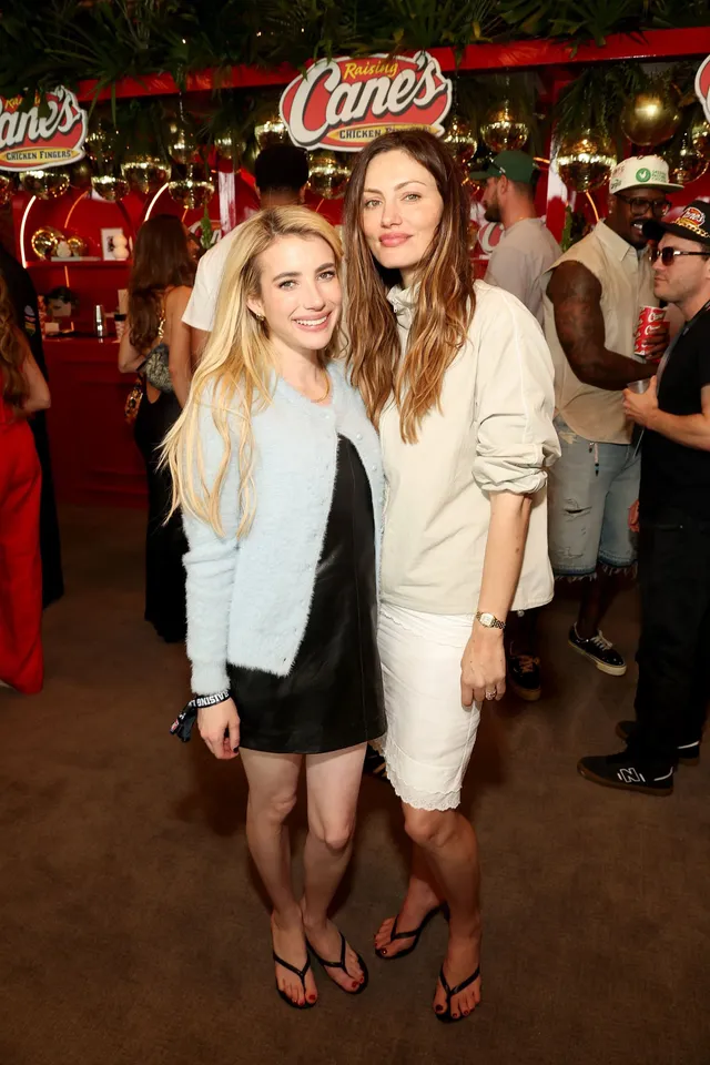 Phoebe Tonkin standing with a companion in a pale outfit and flip-flops.