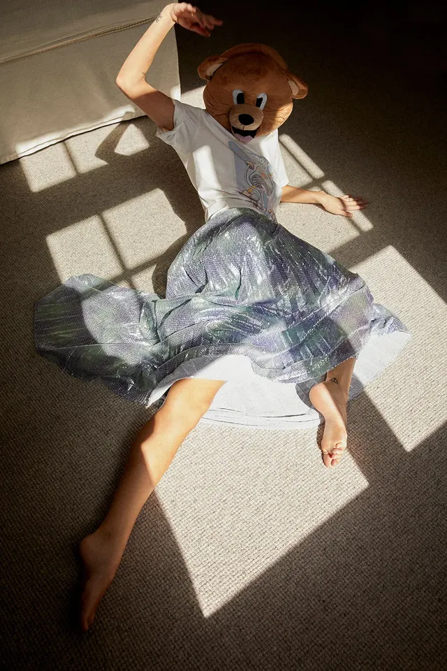 Samara Weaving lying barefoot on a carpet while wearing a bear mask.