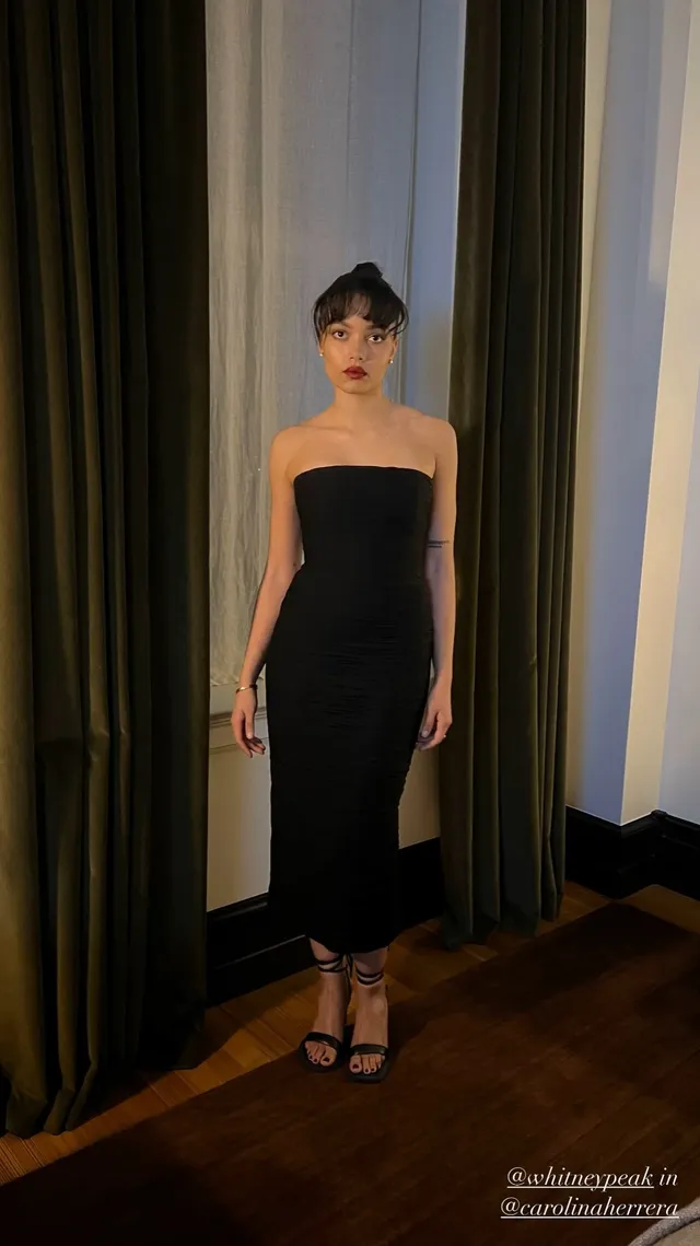 Whitney Peak posing in a long black strapless dress and black heels.