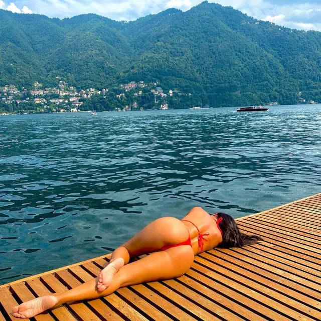 Nicole Scherzinger lying barefoot on a wooden platform beside a lake.