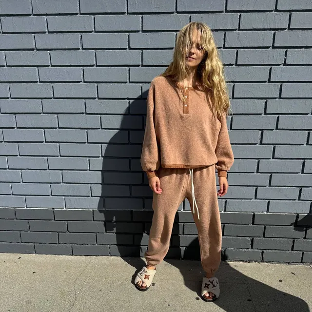 Teresa Palmer standing outside in a tan casual outfit and flat slides.