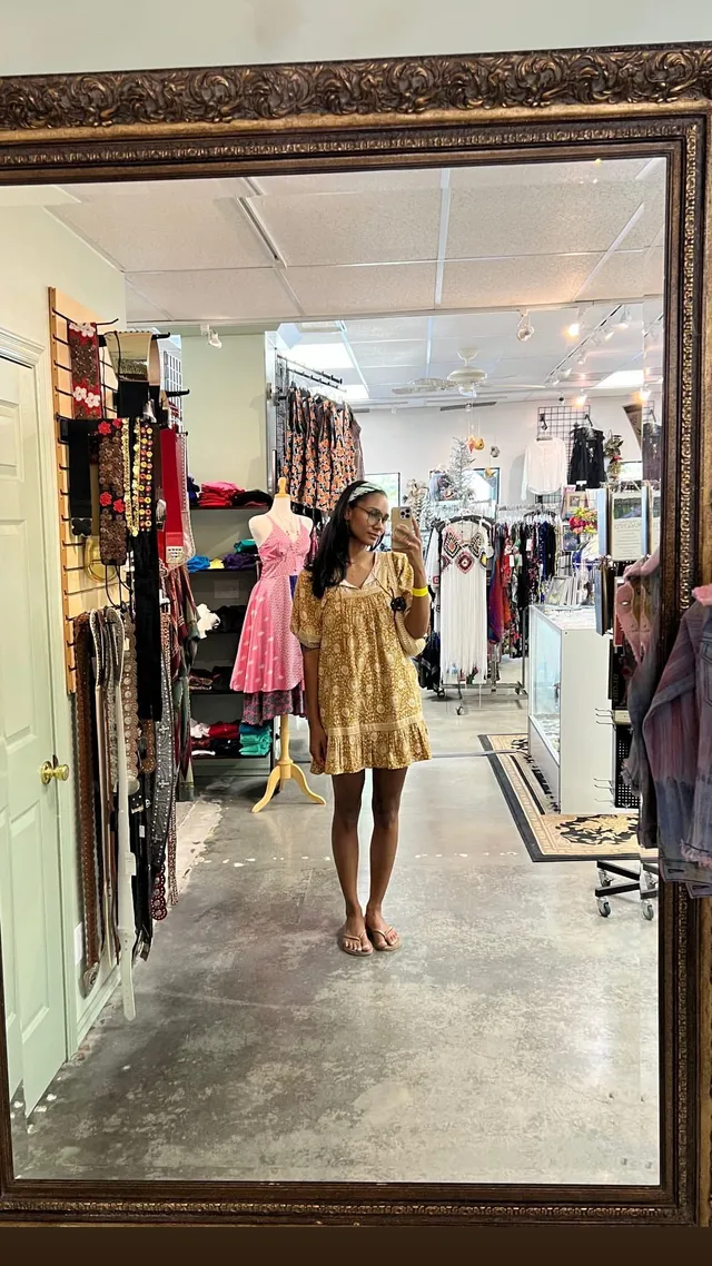 Greta Onieogou taking a mirror selfie in a yellow patterned dress and flat sandals.