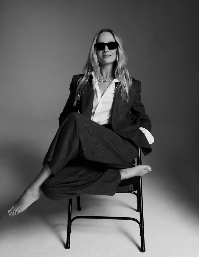 Uma Thurman sitting barefoot in a dark suit and sunglasses.