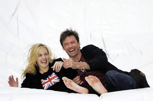Kate Winslet reclining barefoot on a white background beside a companion.