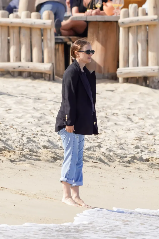 Natalie Portman standing barefoot on the beach in cropped jeans.
