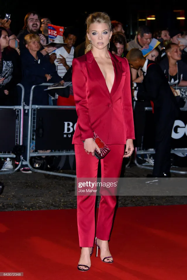 Natalie Dormer standing on a red carpet in a red trouser suit.