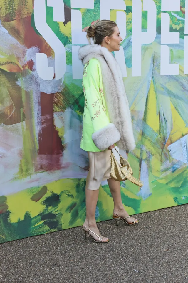 Sienna Miller posing at a fashion show in a bright coat.