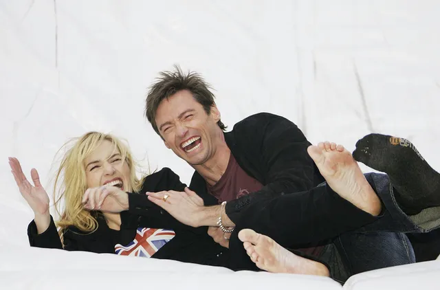 Kate Winslet reclining barefoot beside a companion on a white background.