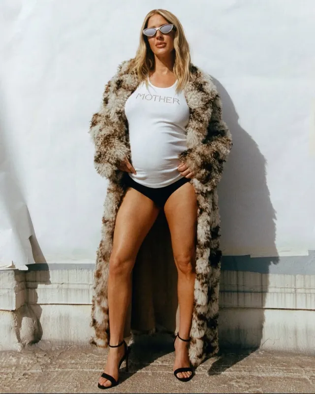 Ellie Goulding standing outdoors in a coat, dark outfit and black heels.