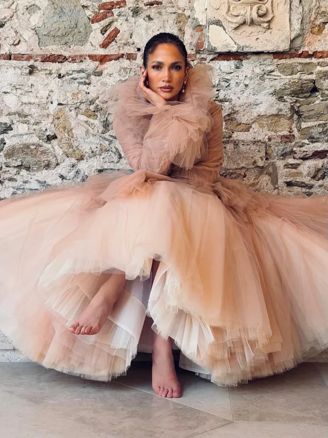 Jennifer Lopez a seated pale tulle dress with bare feet.