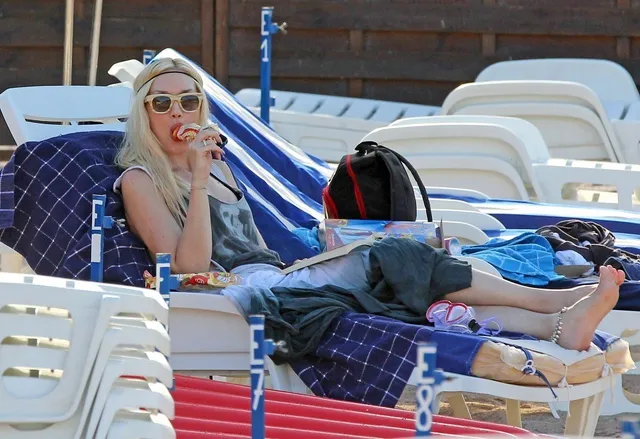 Gwen Stefani reclining barefoot on an outdoor lounger.