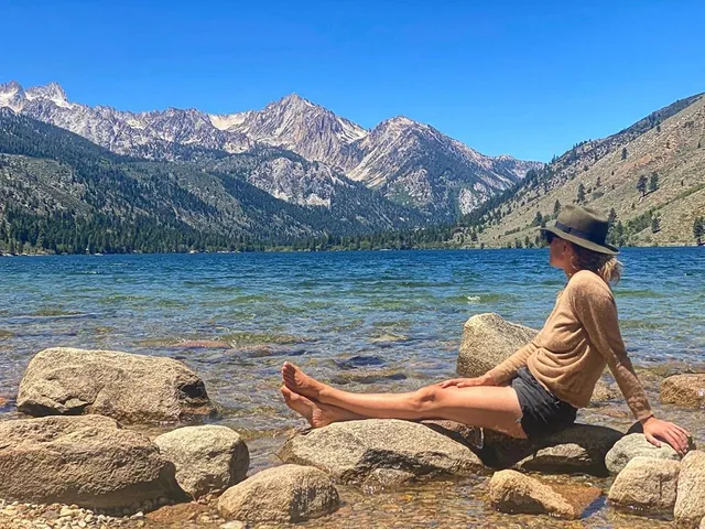 Yvonne Strahovski sitting on rocks beside a mountain lake.